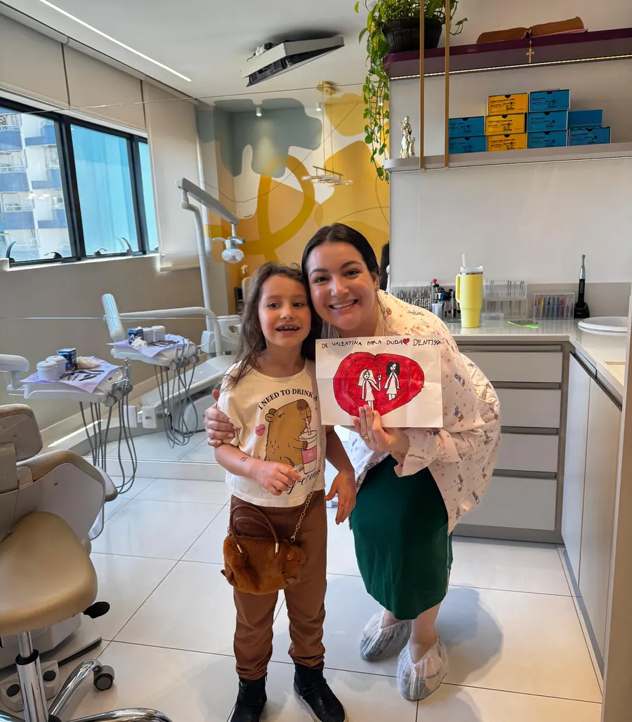 Dra. Eduarda Dagostin com uma pequena paciente, que mostra um desenho feito para ela